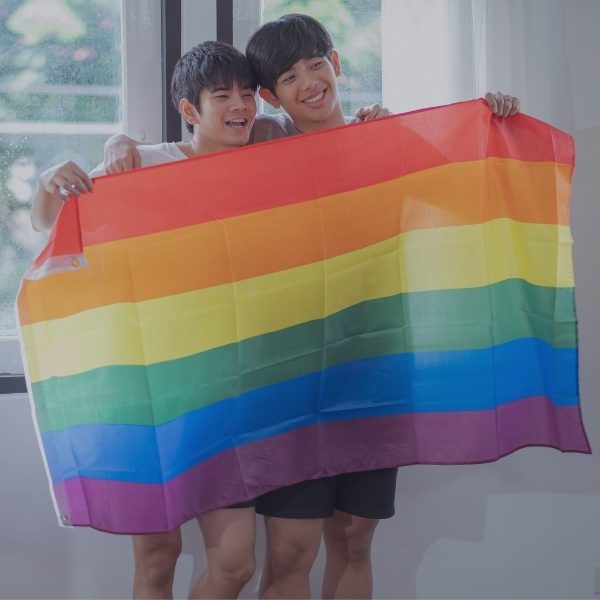 two asian male teenagers holding up a rainbow flag
