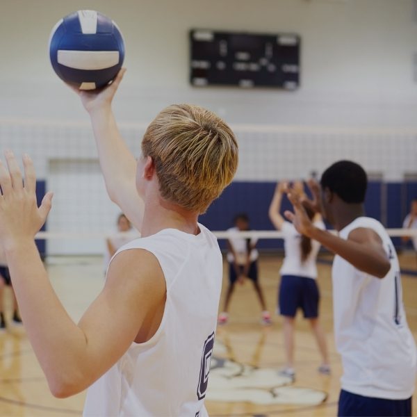back of male student about to serve a volleyball